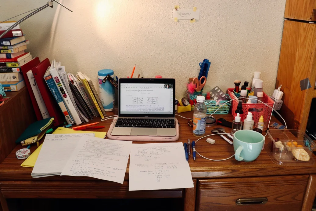 Cluttered dorm desk with makeup scattered across the surface