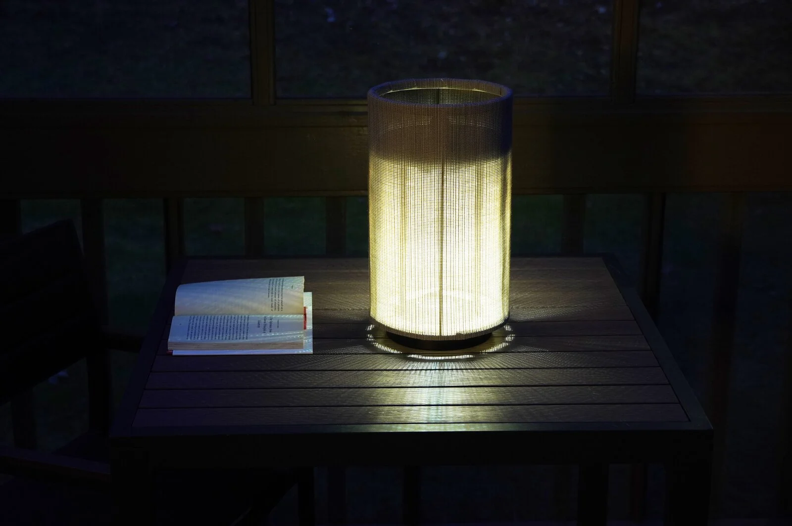 Pelma lamp glowing warmly on a screened porch table at night, casting light across an open book