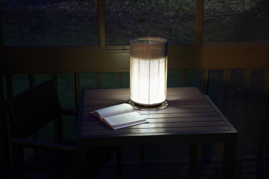 Pelma lamp on an outdoor table with a book, glowing at dusk
