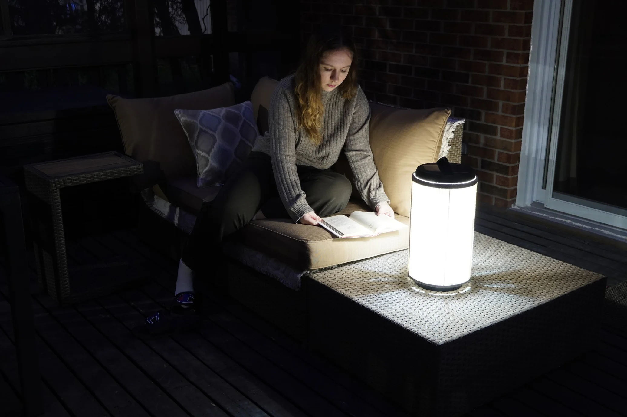 Andrea reading on an outdoor sofa at night, Pelma lamp glowing on the table in front of her