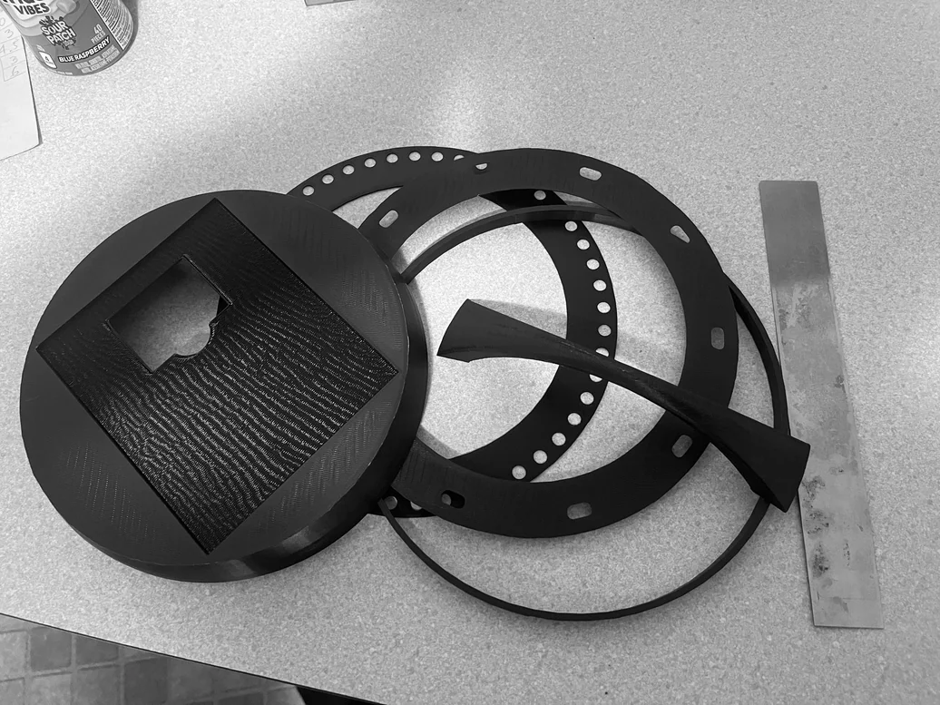 Final 3D-printed components laid out — top cap, fabric-retaining rings, spring steel strip