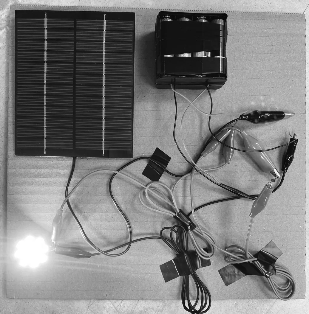 First circuit proof-of-concept — solar panel, battery pack, alligator clips, lit LED