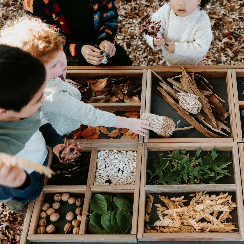 Child exploring compartmentalized wooden boxes filled with natural materials