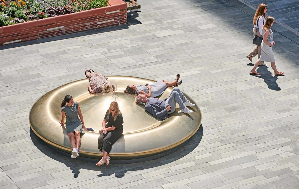 People sitting and lounging on a large circular gold public sculpture