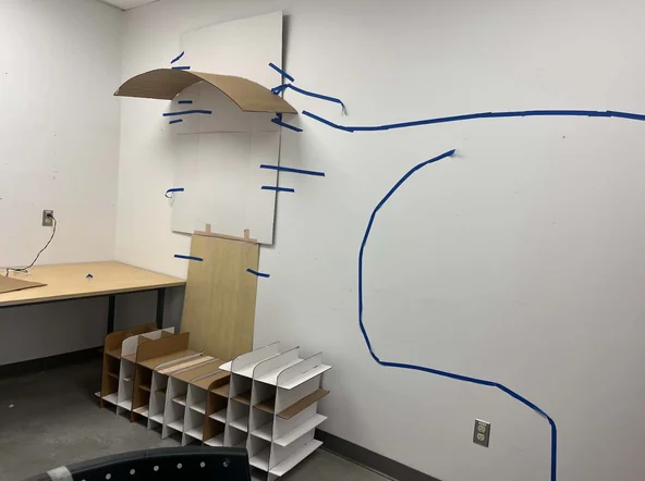 Full-scale cardboard and tape mockup of the shelter form taped to a studio wall
