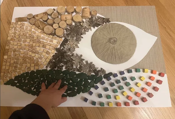 Leaf-shaped sensory panel prototype with mosaic, wood-round, metallic-leaf, stone, and color-block tactile zones
